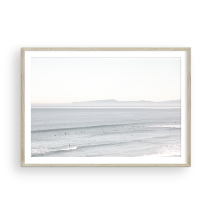 Coastal photography featuring a calm ocean scene with gentle waves and a hazy horizon line, predominantly in blue and white tones. Photograph in minimalist mock up.