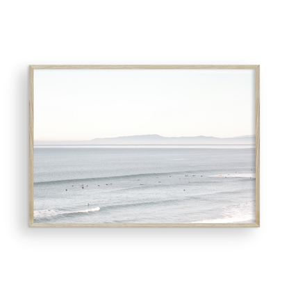 Coastal photography featuring a calm ocean scene with gentle waves and a hazy horizon line, predominantly in blue and white tones. Photograph in minimalist mock up.