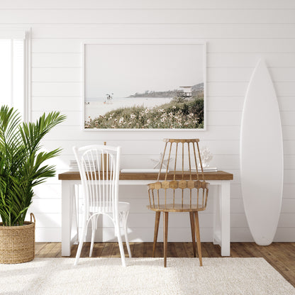 Landscape coastal photography of Salt Creek Beach Park, featuring a lifeguard tower and white flowers in the foreground, with distant cliffs. This calm beach print offers a serene coastal vibe. Photograph in minimalist mock up.