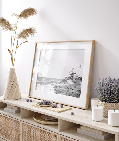 Fine art of WindanSea Beach, La Jolla California horizontal landscape black and white print by Southern California photographer Kim Dybczak of Salt Creek Prints, featuring a powerful waves crashing against the rocky shore of California coast. Beach homes and palm trees sit atop the cliffside, with stairs leading down to a sheltered area. Photograph in minimalist mock up