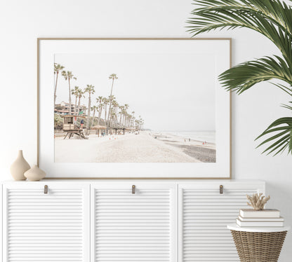 A wide landscape coastal photography view of San Clemente State Beach in Southern California, featuring a row of tall palm trees, a lifeguard tower, and people enjoying the calm beach. This horizontal image evokes Summer Vibes Wall Art and tropical beach print aesthetics. Photograph in minimalist mock up.