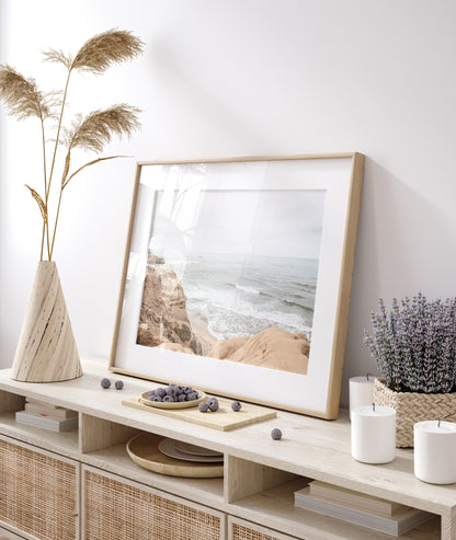 Fine art of Sunset Cliffs, San Diego California horizontal print of hazy high-angle landscape beach photography captures a light blue ocean meeting tall tan and brown cliffs rise as iconic coastal scenery. Photograph in minimalist mock up.