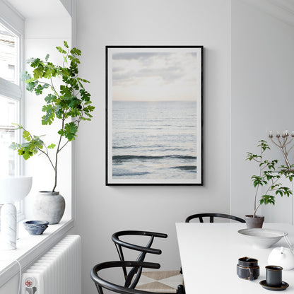 Fine art of vertical landscape print by Southern California photographer Kim Dybczak of Salt Creek Prints, featuring a bright image capturing pale blue ocean waves, light gray clouds in a bright sky. Gentle, small waves in the near and far distance. The sky is a uniform, pale white, creating a soft, overcast atmosphere. Photograph in framed minimalist mock up