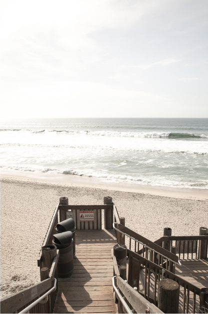 Vertical coastal wall print featuring a stairway leading down to a beach, overlooking an ocean view. 