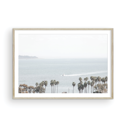 Landscape San Diego beach print showing a seascape with a boat gliding on the water with palm trees in the foreground. Photograph in minimalist mock up.