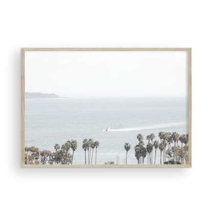 Landscape San Diego beach print showing a seascape with a boat gliding on the water with palm trees in the foreground. Photograph in minimalist mock up.