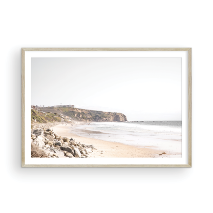 Minimalist ocean print of ocean waves with beach goers in the distance and large  sandy cliffs in the distance overlooking the seascape. Photograph in minimalist mock up.