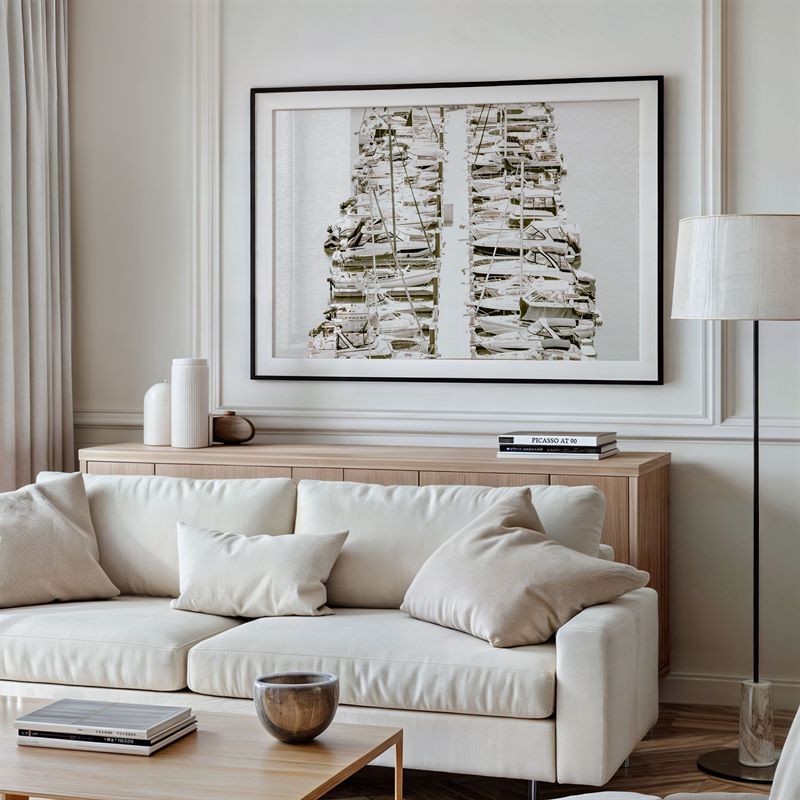 Modern living room with a white sofa, wooden coffee table, and framed photo of a harbor scene on the wall.
