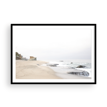 Horizontal coastal photography featuring a beach scene with calm ocean waves and a white sky, with rocks in the distance, located in Laguna California. Photograph in minimalist mock up.