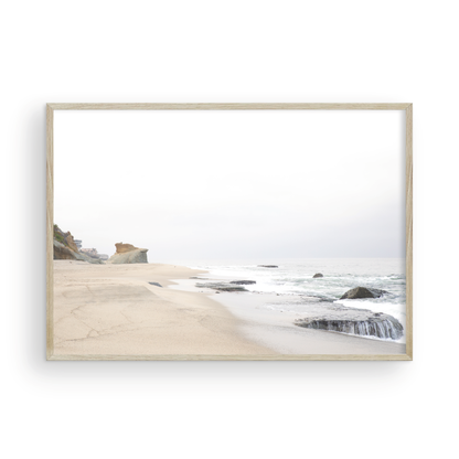Horizontal coastal photography featuring a beach scene with calm ocean waves and a white sky, with rocks in the distance, located in Laguna California. Photograph in minimalist mock up.