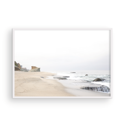Horizontal coastal photography featuring a beach scene with calm ocean waves and a white sky, with rocks in the distance, located in Laguna California. Photograph in minimalist mock up.