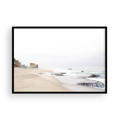 Horizontal coastal photography featuring a beach scene with calm ocean waves and a white sky, with rocks in the distance, located in Laguna California. Photograph in minimalist mock up.
