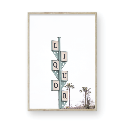 A vertical shot of the iconic Leucadia Liquor sign, with each letter of "LIQUOR" in a separate box against a teal-colored post and a bright white sky with palm trees in the background. Photograph in minimalist mock up