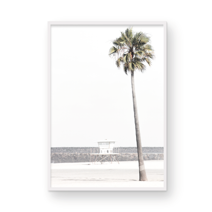 Dreamy coastal palm tree print featuring a tall palm tree in the foreground and a pastel blue lifeguard tower centered in the distance. This vertical tropical print is captured at Oceanside Beach on the Southern California coast, is bathed in bright, hazy sunlight, creating a pastel beach art effect. Photograph in minimalist mock up.
