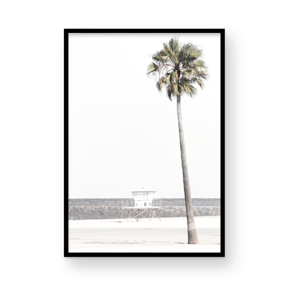Dreamy coastal palm tree print featuring a tall palm tree in the foreground and a pastel blue lifeguard tower centered in the distance. This vertical tropical print is captured at Oceanside Beach on the Southern California coast, is bathed in bright, hazy sunlight, creating a pastel beach art effect. Photograph in minimalist mock up.