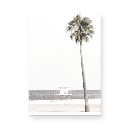Dreamy coastal palm tree print featuring a tall palm tree in the foreground and a pastel blue lifeguard tower centered in the distance. This vertical tropical print is captured at Oceanside Beach on the Southern California coast, is bathed in bright, hazy sunlight, creating a pastel beach art effect. Photograph in minimalist mock up.