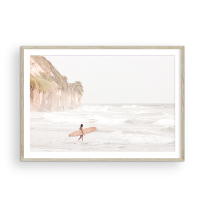 Horizontal surf art print of a lone surfer carrying a surfboard, walking on a rocky, foggy shoreline at Moonlight State Beach with a cliff in the background. Photograph in minimalist mock up.