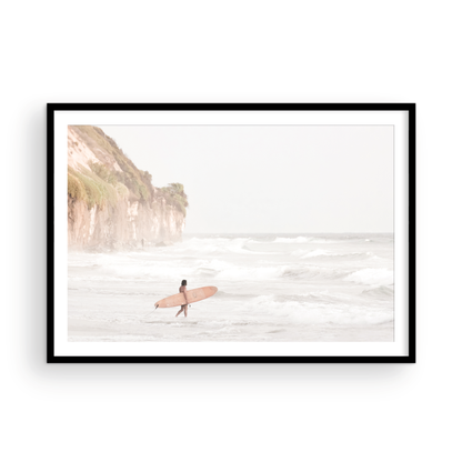 Horizontal surf art print of a lone surfer carrying a surfboard, walking on a rocky, foggy shoreline at Moonlight State Beach with a cliff in the background. Photograph in minimalist mock up.