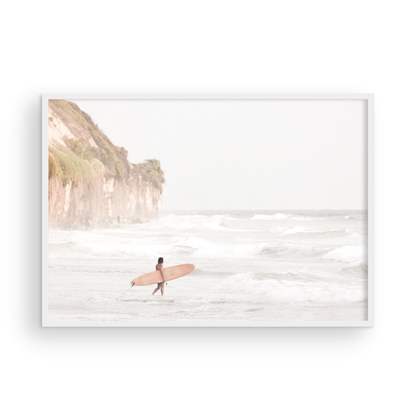 Horizontal surf art print of a lone surfer carrying a surfboard, walking on a rocky, foggy shoreline at Moonlight State Beach with a cliff in the background. Photograph in minimalist mock up.
