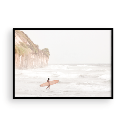 Horizontal surf art print of a lone surfer carrying a surfboard, walking on a rocky, foggy shoreline at Moonlight State Beach with a cliff in the background. Photograph in minimalist mock up.