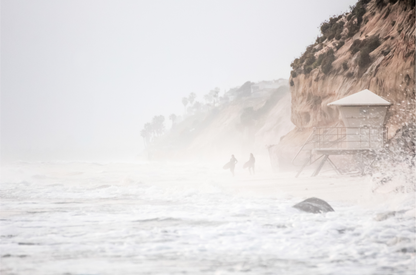 Hazy surf art of two surfers running into stormy ocean waves at Moonlight State Beach, with a lifeguard tower and cliff disappearing into the fog. A dramatic seascape print.