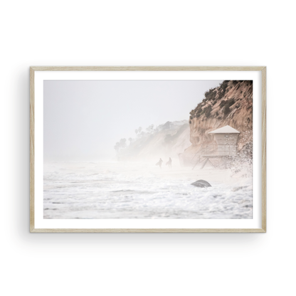 Hazy surf art of two surfers running into stormy ocean waves at Moonlight State Beach, with a lifeguard tower and cliff disappearing into the fog. A dramatic seascape print. Photograph in minimalist mock up
