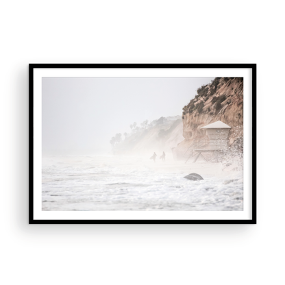 Hazy surf art of two surfers running into stormy ocean waves at Moonlight State Beach, with a lifeguard tower and cliff disappearing into the fog. A dramatic seascape print. Photograph in minimalist mock up