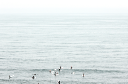 Horizontal surf art showing multiple surfers waiting in the calm ocean water for waves, with a hazy Southern California coastline in the distance. This minimalist surf print captures authentic surf vibes. 