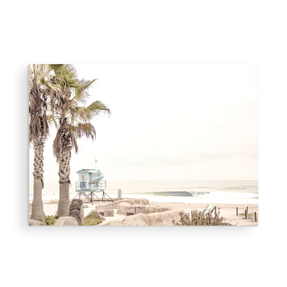 Dreamy coastal palm tree print featuring two tall palm trees with shaggy trunks in the foreground and a pastel blue lifeguard tower in the distance. This horizontal tropical print is captured at Seaside Beach on the Southern California coast, is bathed in bright, hazy sunlight, creating a pastel beach art effect. Evokes serene summer vibes, perfect for beach house decor. Photograph in minimalist mock up.