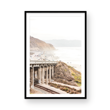 Captivating Torrey Pines San Diego coast scene, presented as vertical beach art. This piece of travel photography features a prominent bridge extending over a wide sandy beach with calm ocean waves. A coastal road winds along the base of rugged cliffs, with a lone coastal palm tree adding a touch of tropical essence to this Southern California seascape print. Photograph in minimalist mock up