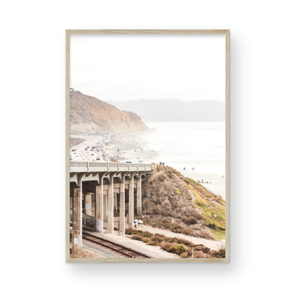 Captivating Torrey Pines San Diego coast scene, presented as vertical beach art. This piece of travel photography features a prominent bridge extending over a wide sandy beach with calm ocean waves. A coastal road winds along the base of rugged cliffs, with a lone coastal palm tree adding a touch of tropical essence to this Southern California seascape print. Photograph in minimalist mock up
