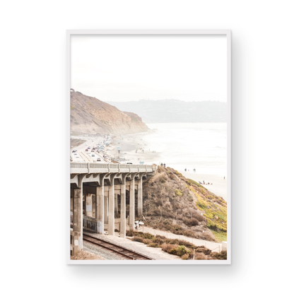 Captivating Torrey Pines San Diego coast scene, presented as vertical beach art. This piece of travel photography features a prominent bridge extending over a wide sandy beach with calm ocean waves. A coastal road winds along the base of rugged cliffs, with a lone coastal palm tree adding a touch of tropical essence to this Southern California seascape print. Photograph in minimalist mock up