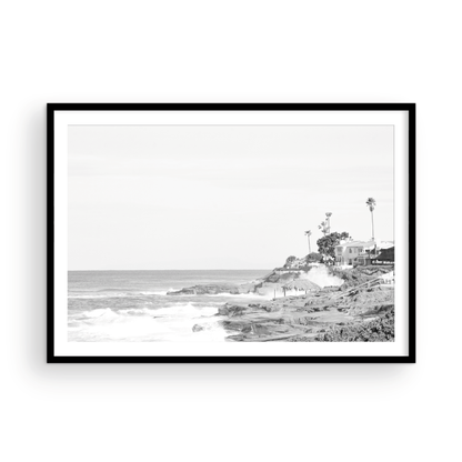 Fine art of WindanSea Beach, La Jolla California horizontal landscape black and white print by Southern California photographer Kim Dybczak of Salt Creek Prints, featuring a powerful waves crashing against the rocky shore of California coast. Beach homes and palm trees sit atop the cliffside, with stairs leading down to a sheltered area. Photograph in minimalist mock up