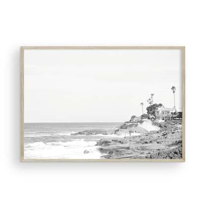 Fine art of WindanSea Beach, La Jolla California horizontal landscape black and white print by Southern California photographer Kim Dybczak of Salt Creek Prints, featuring a powerful waves crashing against the rocky shore of California coast. Beach homes and palm trees sit atop the cliffside, with stairs leading down to a sheltered area. Photograph in minimalist mock up