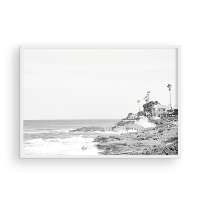 Fine art of WindanSea Beach, La Jolla California horizontal landscape black and white print by Southern California photographer Kim Dybczak of Salt Creek Prints, featuring a powerful waves crashing against the rocky shore of California coast. Beach homes and palm trees sit atop the cliffside, with stairs leading down to a sheltered area. Photograph in minimalist mock up