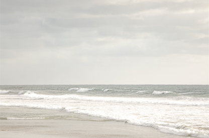 Horizontal minimalist ocean print of gentle ocean waves rolling onto a sandy shoreline at Moonlight Beach, San Diego, under a bright, soft sky. This calm beach print provides a serene seascape. 
