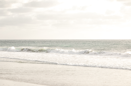 Minimalist ocean print of gentle ocean waves rolling onto a sandy shoreline at Moonlight Beach, San Diego, under a bright, soft sky. This calm beach print provides a serene seascape.