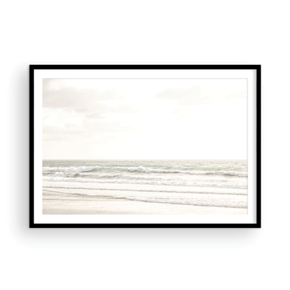 Horizontal minimalist ocean print of gentle ocean waves rolling onto a sandy shoreline at Moonlight Beach, San Diego, under a bright, soft sky. This calm beach print provides a serene seascape. Photograph in minimalist mock up.