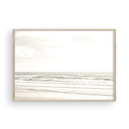 Horizontal minimalist ocean print of gentle ocean waves rolling onto a sandy shoreline at Moonlight Beach, San Diego, under a bright, soft sky. This calm beach print provides a serene seascape. Photograph in minimalist mock up.