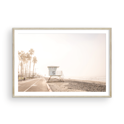 Landscape lifeguard tower photography of Oceanside, California, showing lifeguard tower number 5 on the beach with palm trees and a pathway leading towards the ocean. Photograph in minimalist mock up.