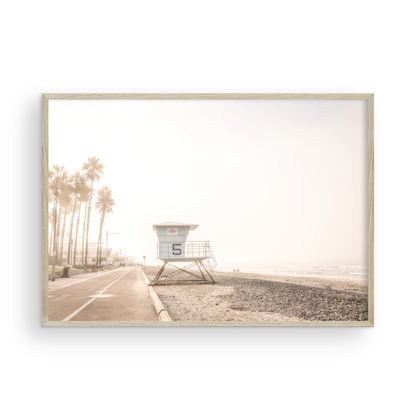 Landscape lifeguard tower photography of Oceanside, California, showing lifeguard tower number 5 on the beach with palm trees and a pathway leading towards the ocean. Photograph in minimalist mock up.