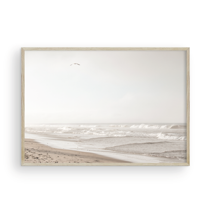 Minimalist ocean print featuring gentle ocean waves breaking on a sandy beach under a bright, hazy sky with a single bird in flight. A serene and neutral ocean print. Photograph in minimalist mock up.