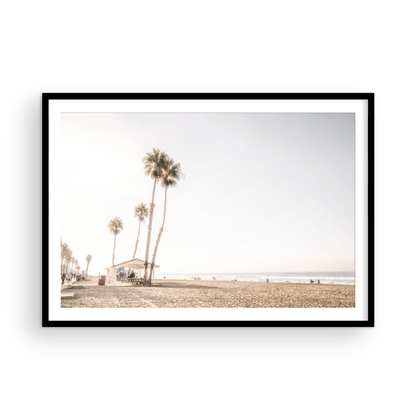 Landscape beach photography of Venice Beach, California, showcasing the sandy beach, ocean, and a small shelter with palm trees along the boardwalk. Captures the casual beach art feel. Photograph in minimalist mock up.