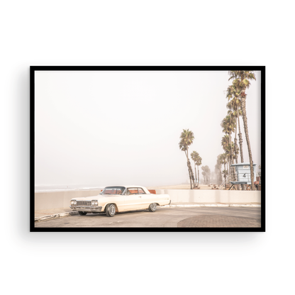 Landscape beach photography featuring a vintage white car parked on a coastal road with tall palm trees and a lifeguard tower nearby, overlooking the ocean. Photograph in minimalist mock up.