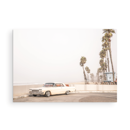 Landscape beach photography featuring a vintage white car parked on a coastal road with tall palm trees and a lifeguard tower nearby, overlooking the ocean. Photograph in minimalist mock up.