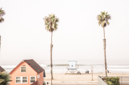 Landscape beach photography of Oceanside, California, highlighting a beachfront house and a lifeguard tower with two tall palm trees and the ocean. 