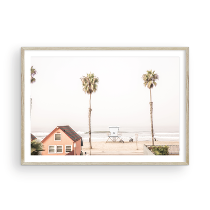 Landscape beach photography of Oceanside, California, highlighting a beachfront house and a lifeguard tower with two tall palm trees and the ocean. Photograph in minimalist mock up.