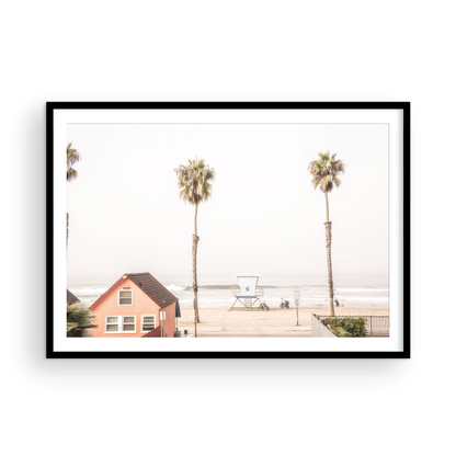 Landscape beach photography of Oceanside, California, highlighting a beachfront house and a lifeguard tower with two tall palm trees and the ocean. Photograph in minimalist mock up.