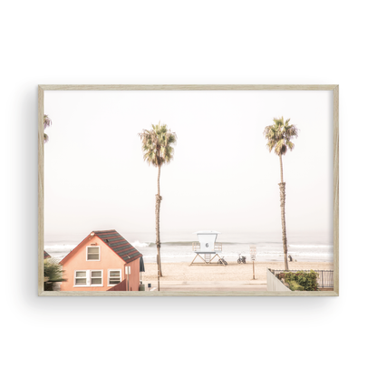 Landscape beach photography of Oceanside, California, highlighting a beachfront house and a lifeguard tower with two tall palm trees and the ocean. Photograph in minimalist mock up.