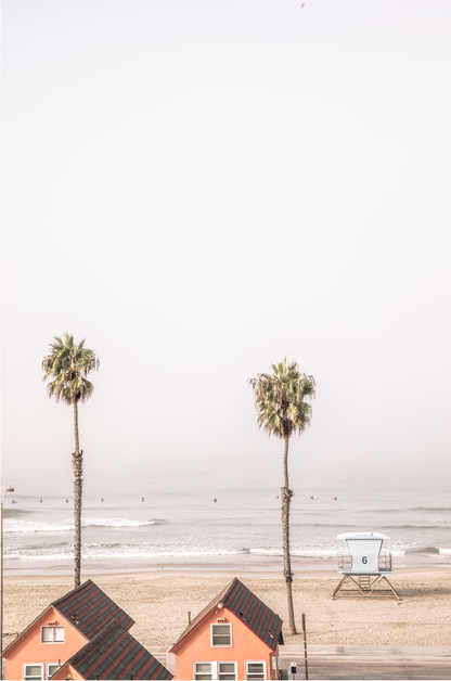 Vertical coastal photography of Oceanside, California, showing beachfront houses and a lifeguard tower with two prominent palm trees overlooking the ocean. A minimalist surf print